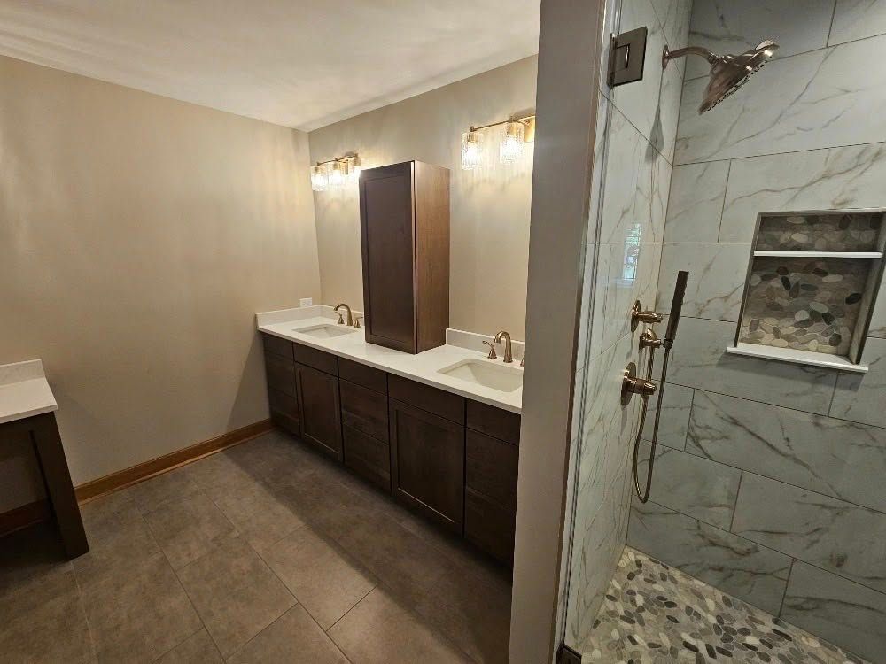 Bathroom featuring a double vanity, shower, and neutral color palette. Brown cabinets and tile.