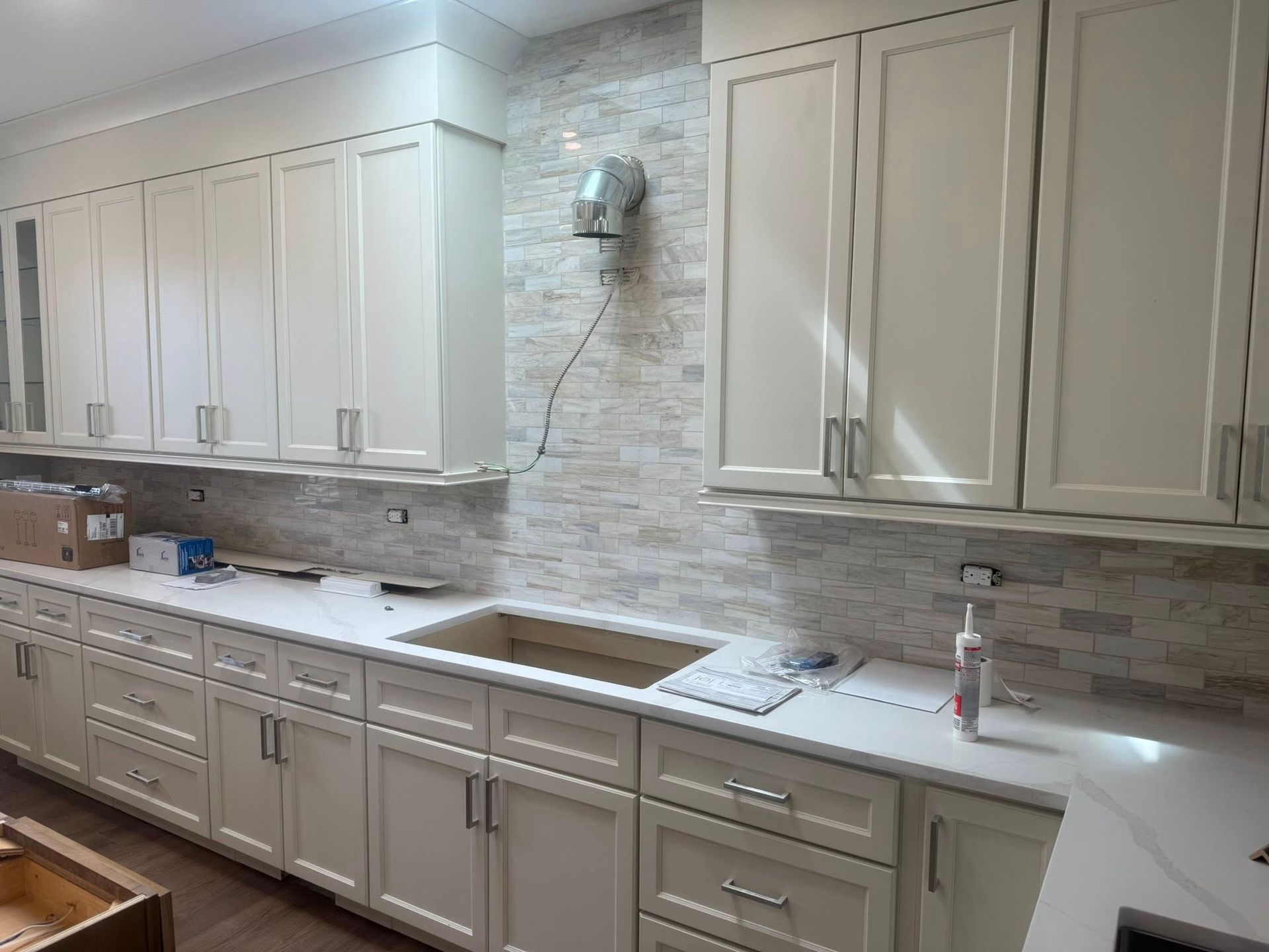 Cream kitchen cabinets with a stone backsplash and white countertops.