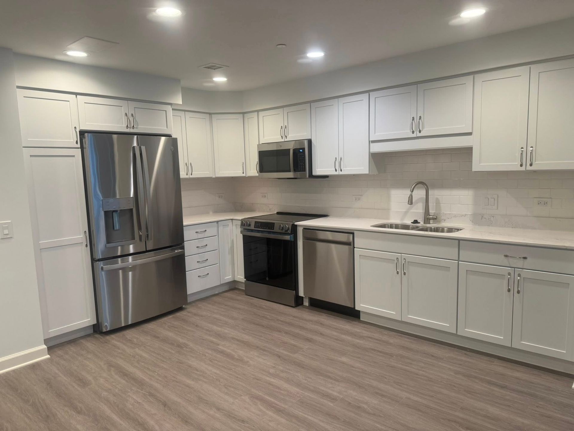 White kitchen with stainless steel appliances, white cabinets, and gray flooring.