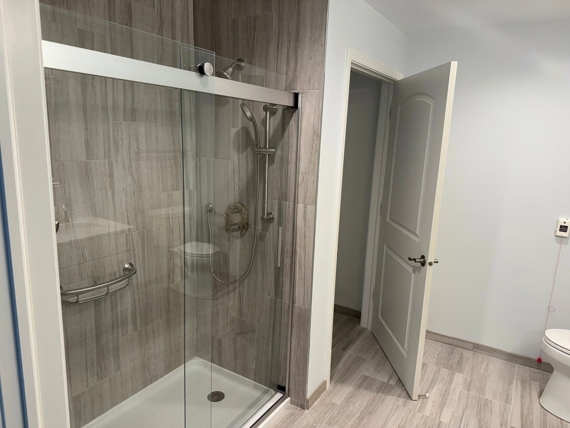 Accessible bathroom with a glass shower, grab bar, and open door.