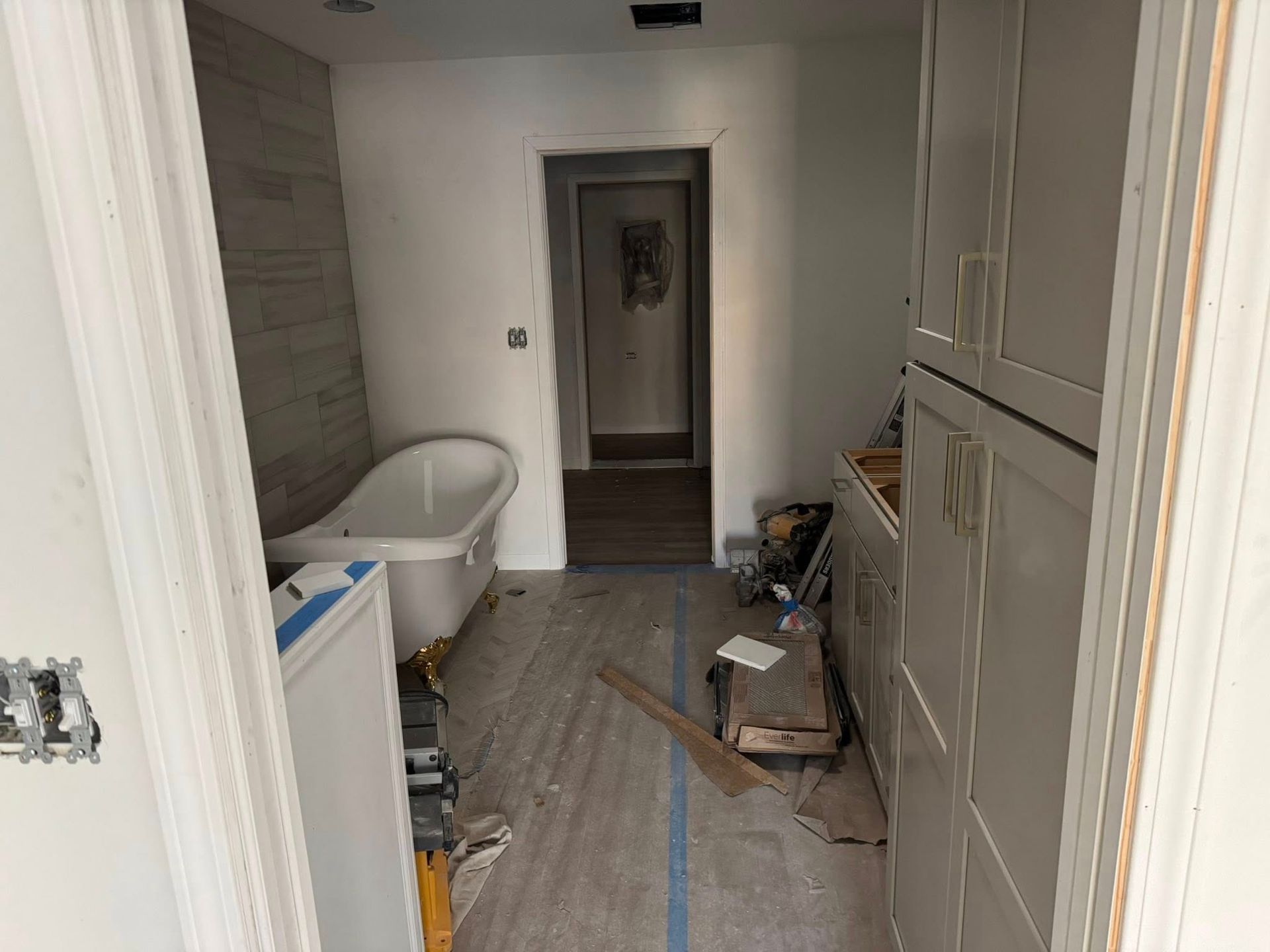Narrow unfinished hallway with bathtub, cabinets, tools, and construction debris