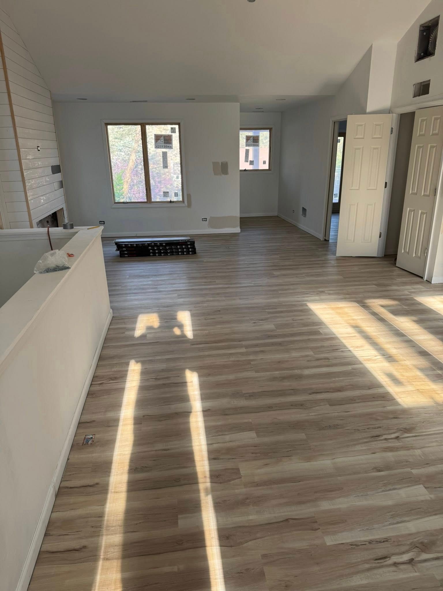 Empty modern room with light wood flooring, white walls, windows, and sunbeams across the floor.