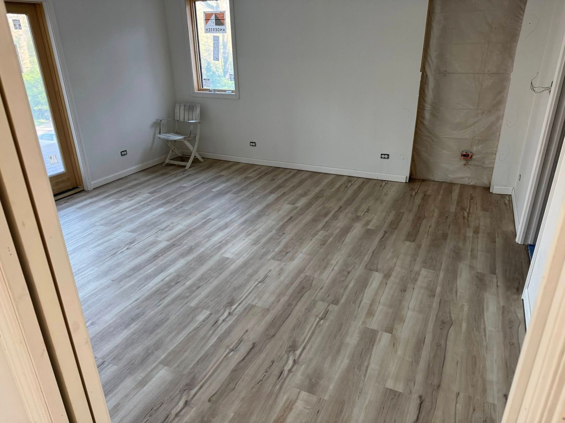 Empty room with light wood flooring, white walls, a small chair, and a window near the back wall