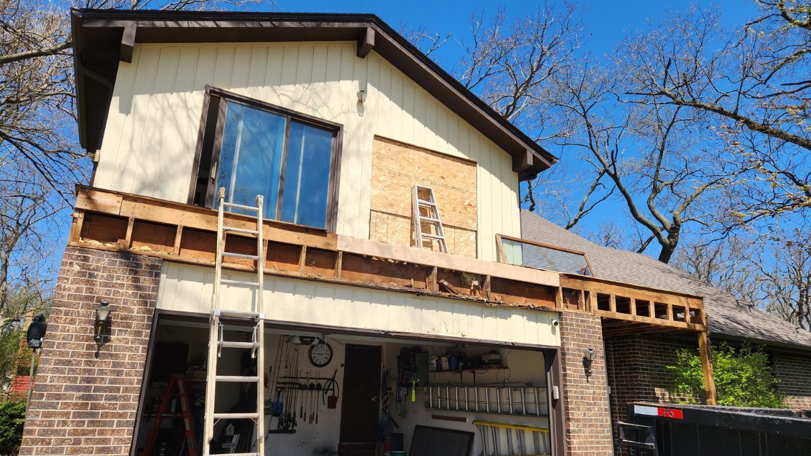 Two-story house under renovation with ladder, exposed wood framing, and blue sky overhead
