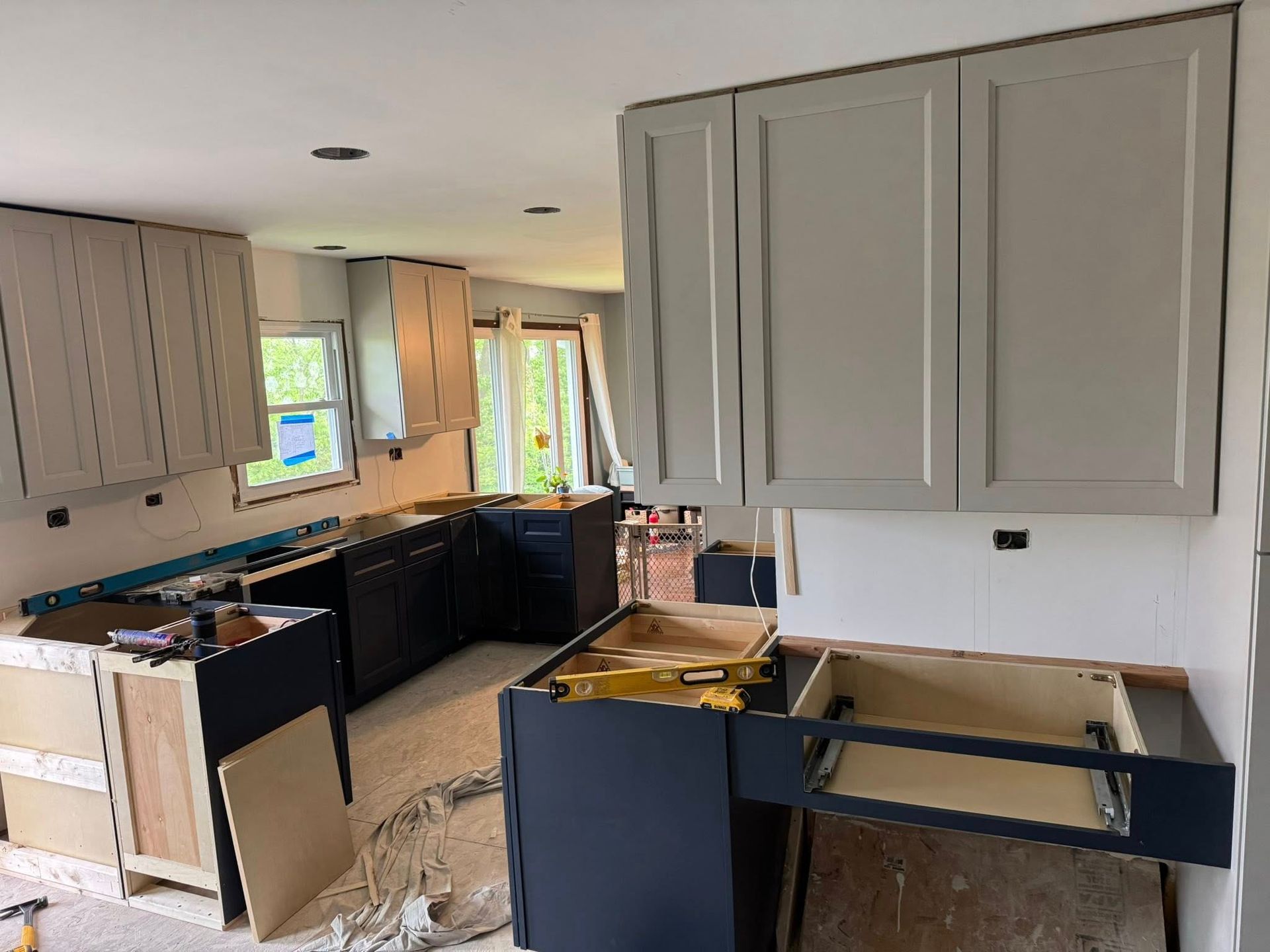 Kitchen under construction with gray and black cabinets, tools, and unfinished walls.