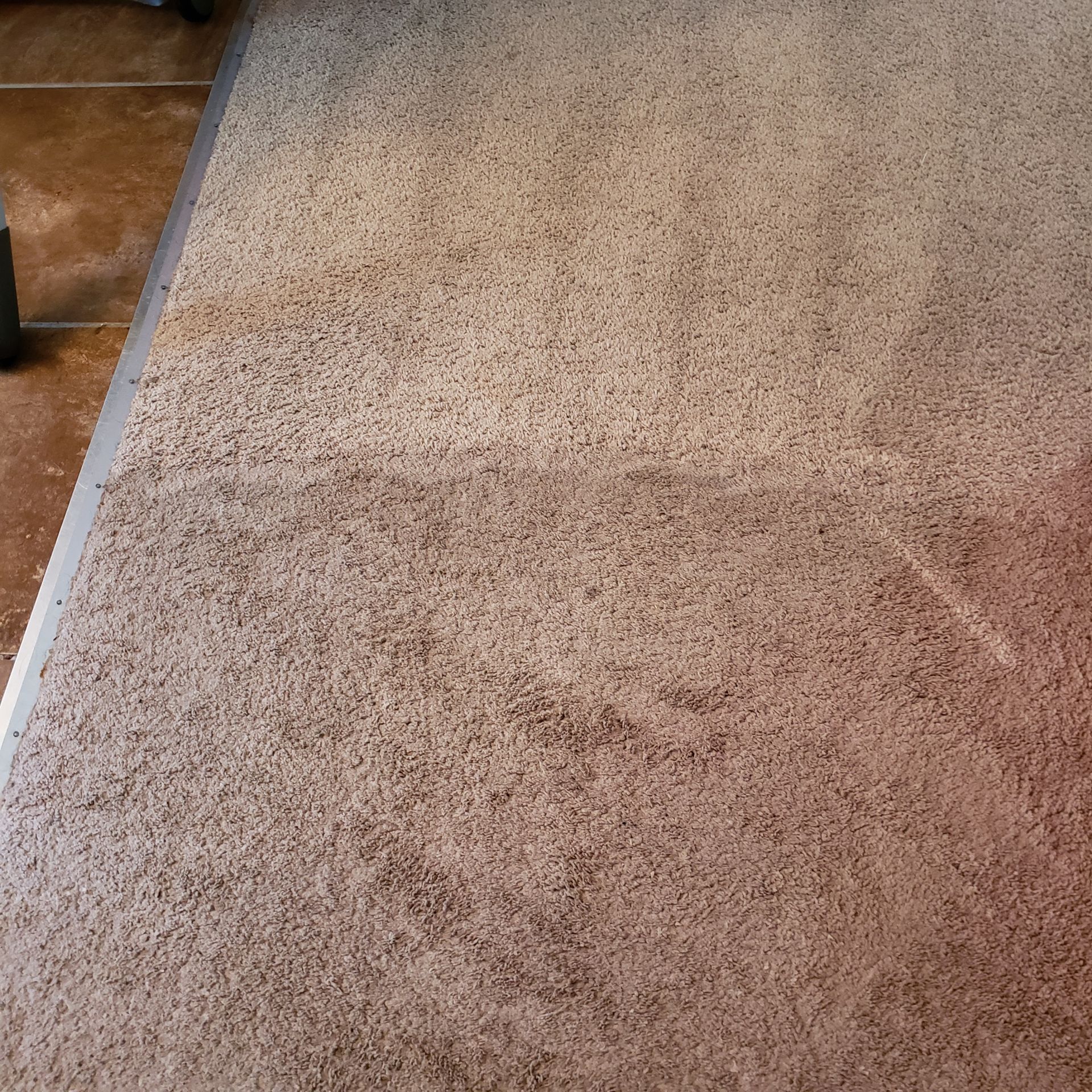a brown carpet is sitting on a tiled floor next to a chair
