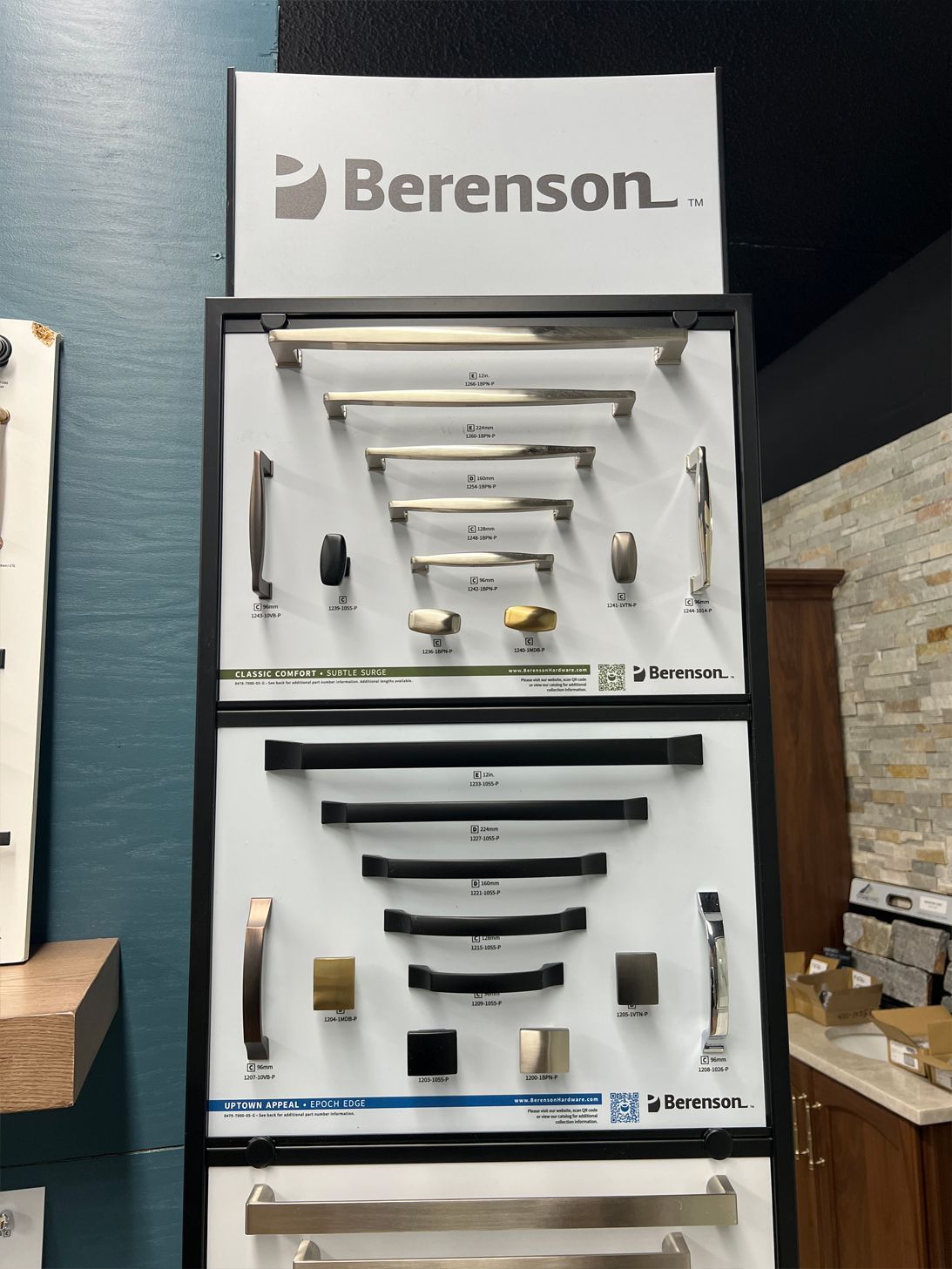Display of Berenson brand cabinet hardware samples in a showroom, featuring various handle and knob styles in metallic finishes.