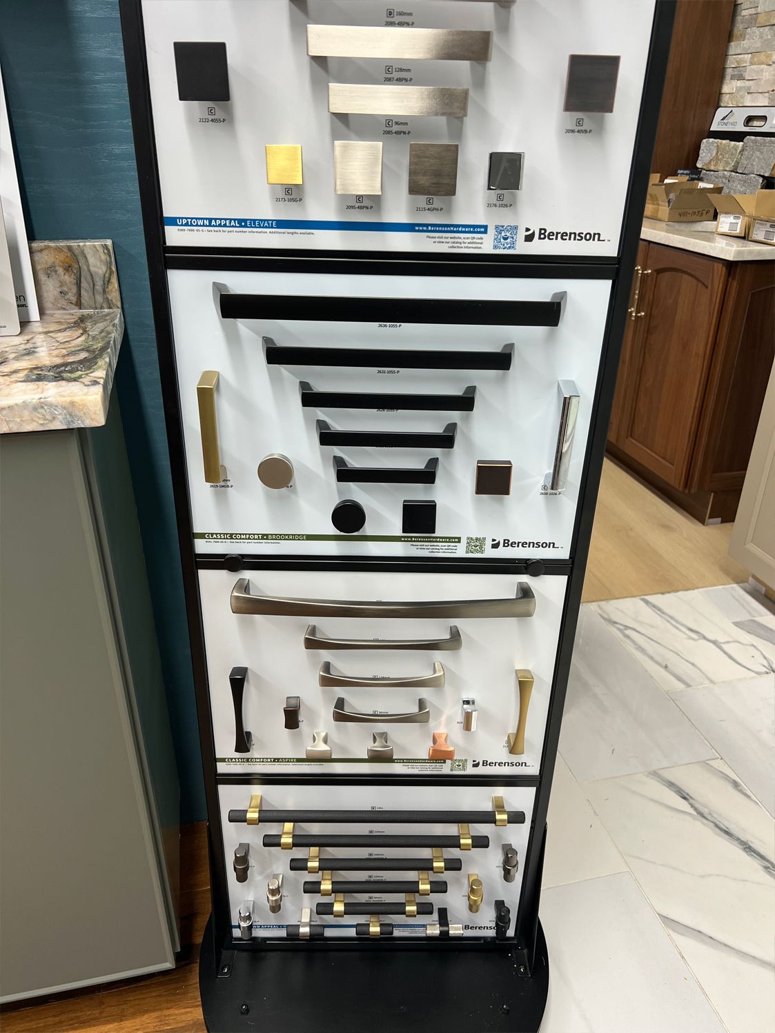 Display of various cabinet hardware samples in a showroom, including pulls, knobs, and finishes like gold and black.