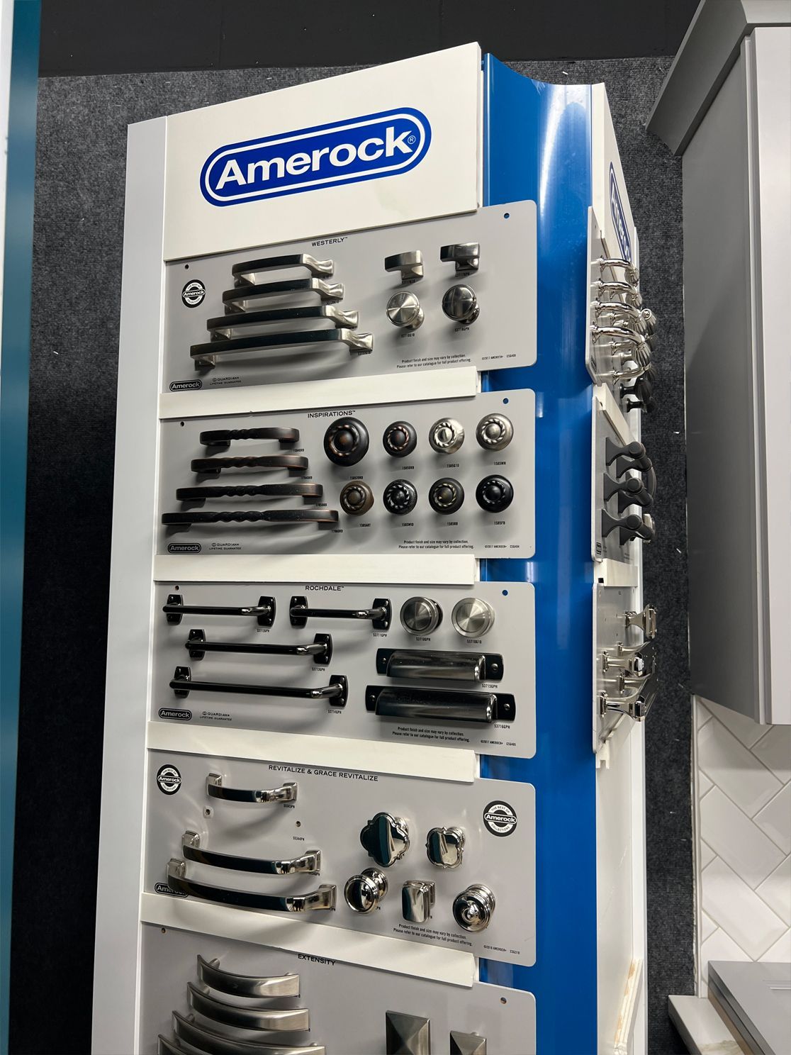 Display of Amerock cabinet hardware samples in a showroom, featuring various handle and knob styles in silver and black finishes.