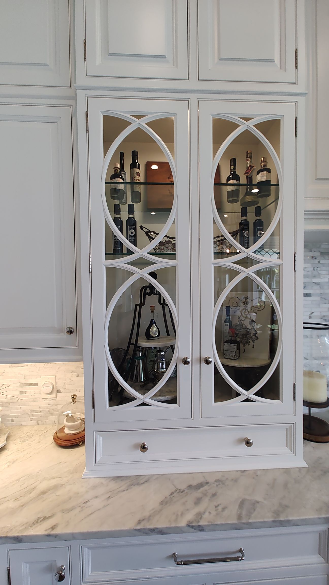 A kitchen with a glass cabinet filled with bottles and glasses.