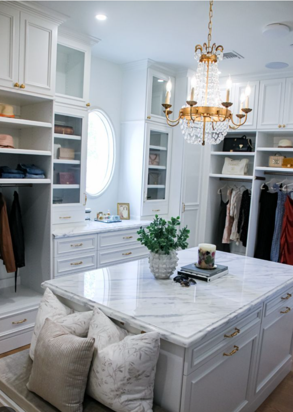 A walk in closet with a large island in the middle and a chandelier.