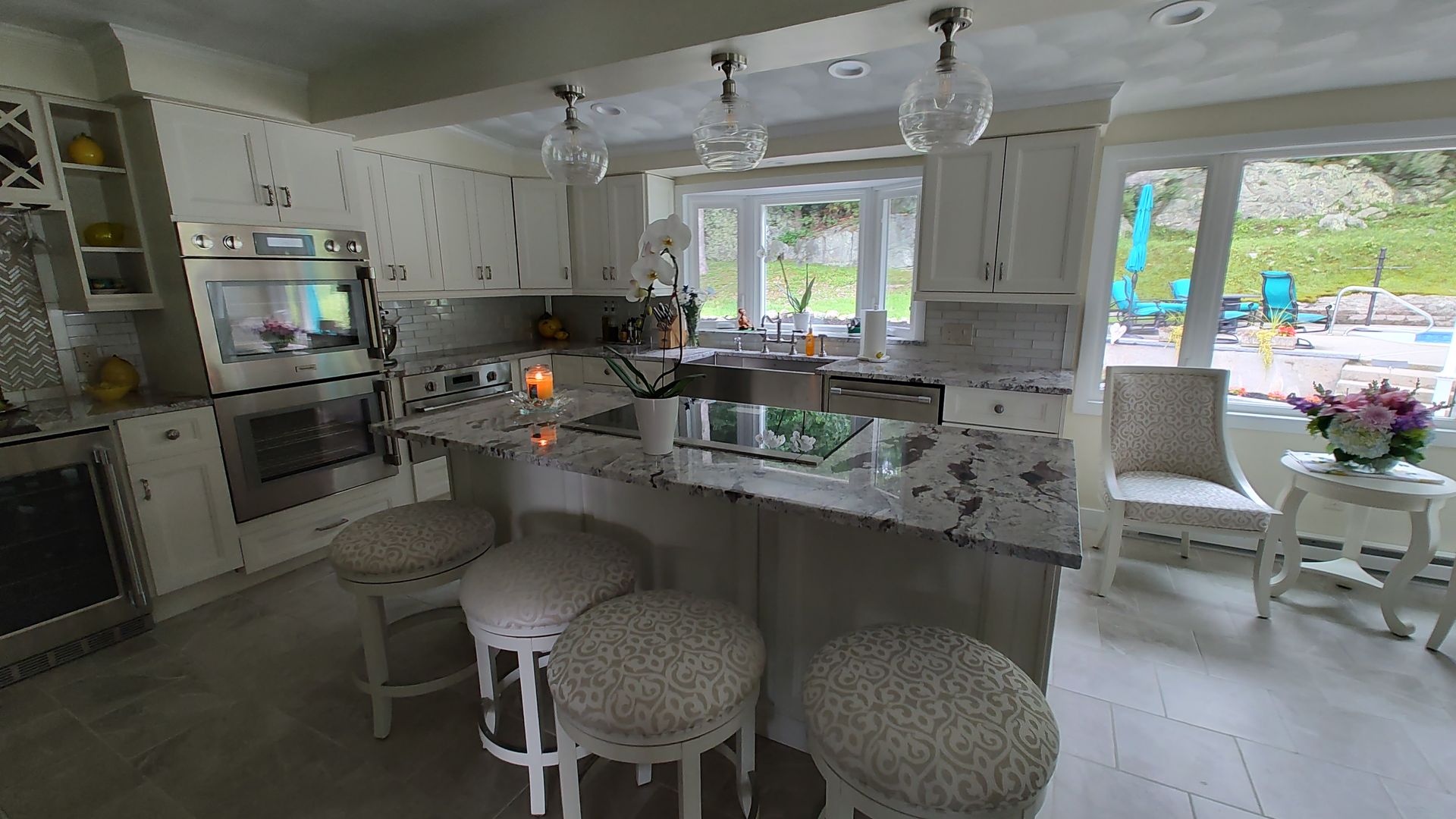 A kitchen with white cabinets, granite countertops, stools, and a large island.