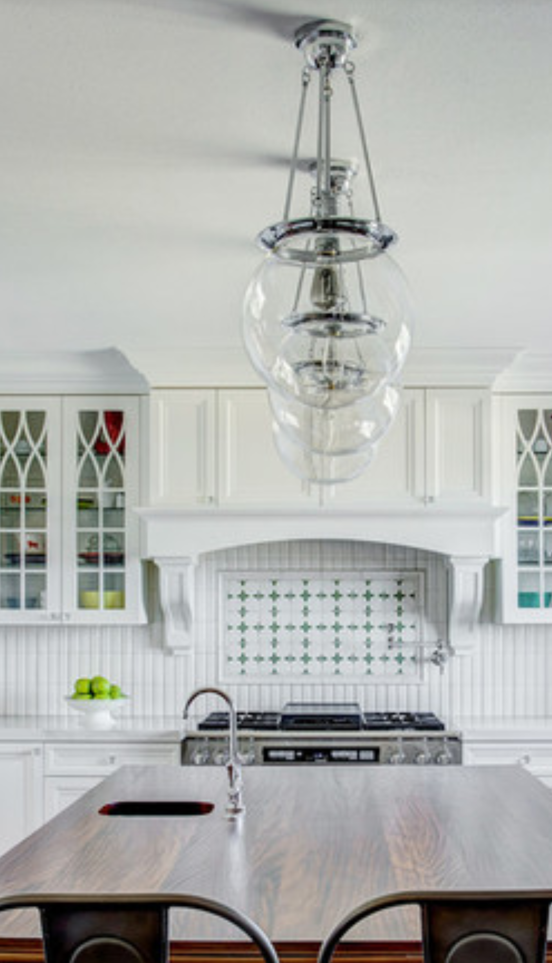 A kitchen with white cabinets, a stove, a sink, and a chandelier hanging from the ceiling.