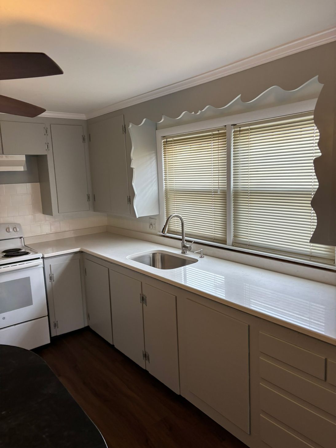 Kitchen with white cabinets, countertop, sink, and blinds.