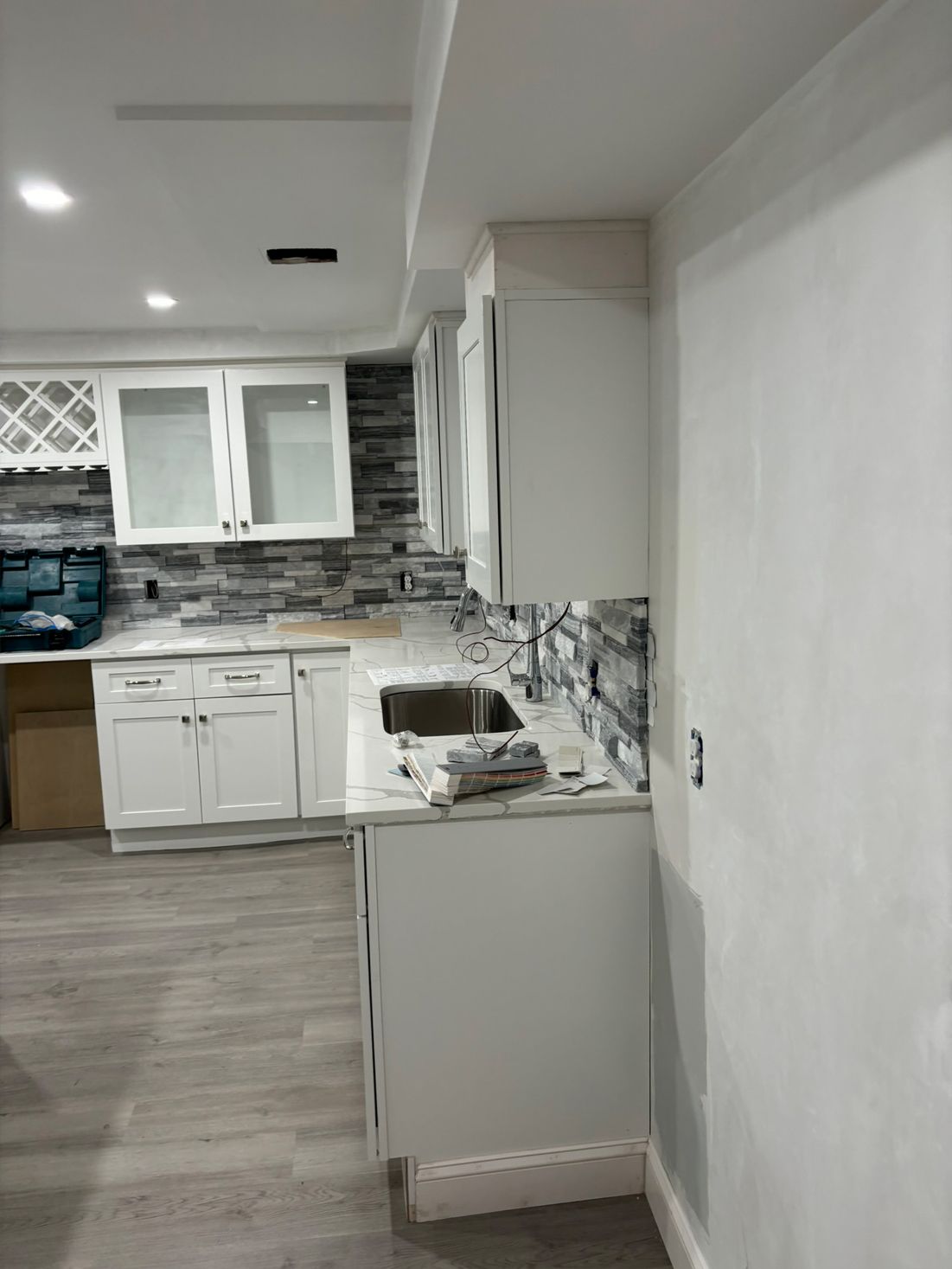 White kitchen cabinets installed in a room with light grey flooring and stone tile backsplash.