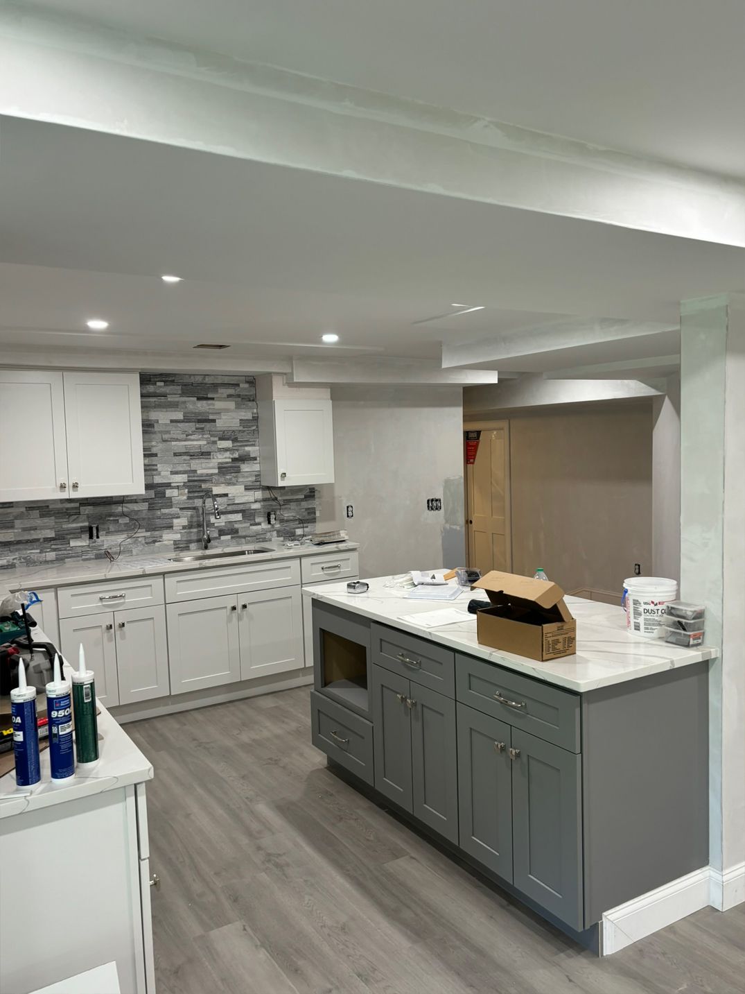 Newly renovated kitchen with gray island and white cabinets. Backsplash is gray and white.