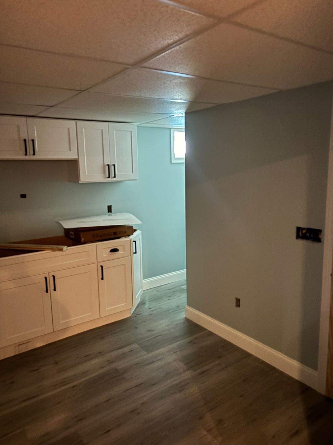 Basement with white cabinets, light blue walls, gray flooring, and a small window.