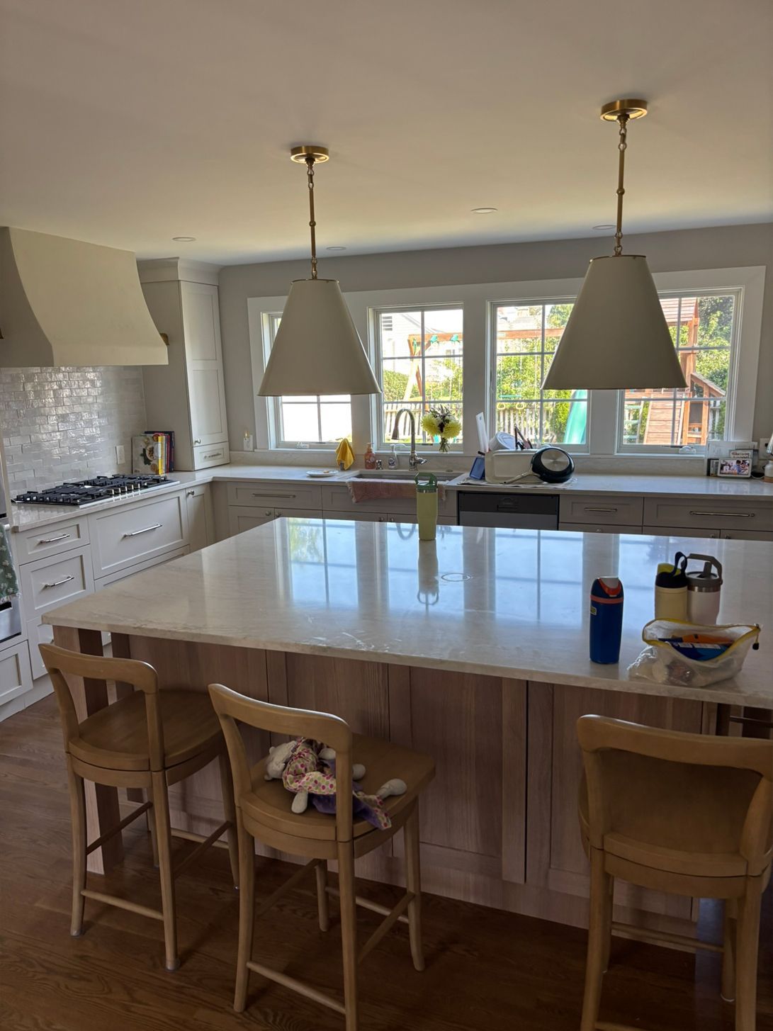Kitchen with large island, pendant lights, and bar stools. Windows in background.