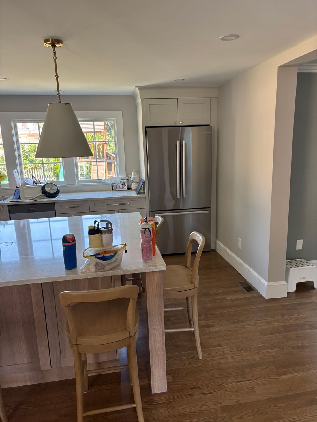 Kitchen with white cabinets, stainless steel refrigerator, island with seating, and wood flooring.