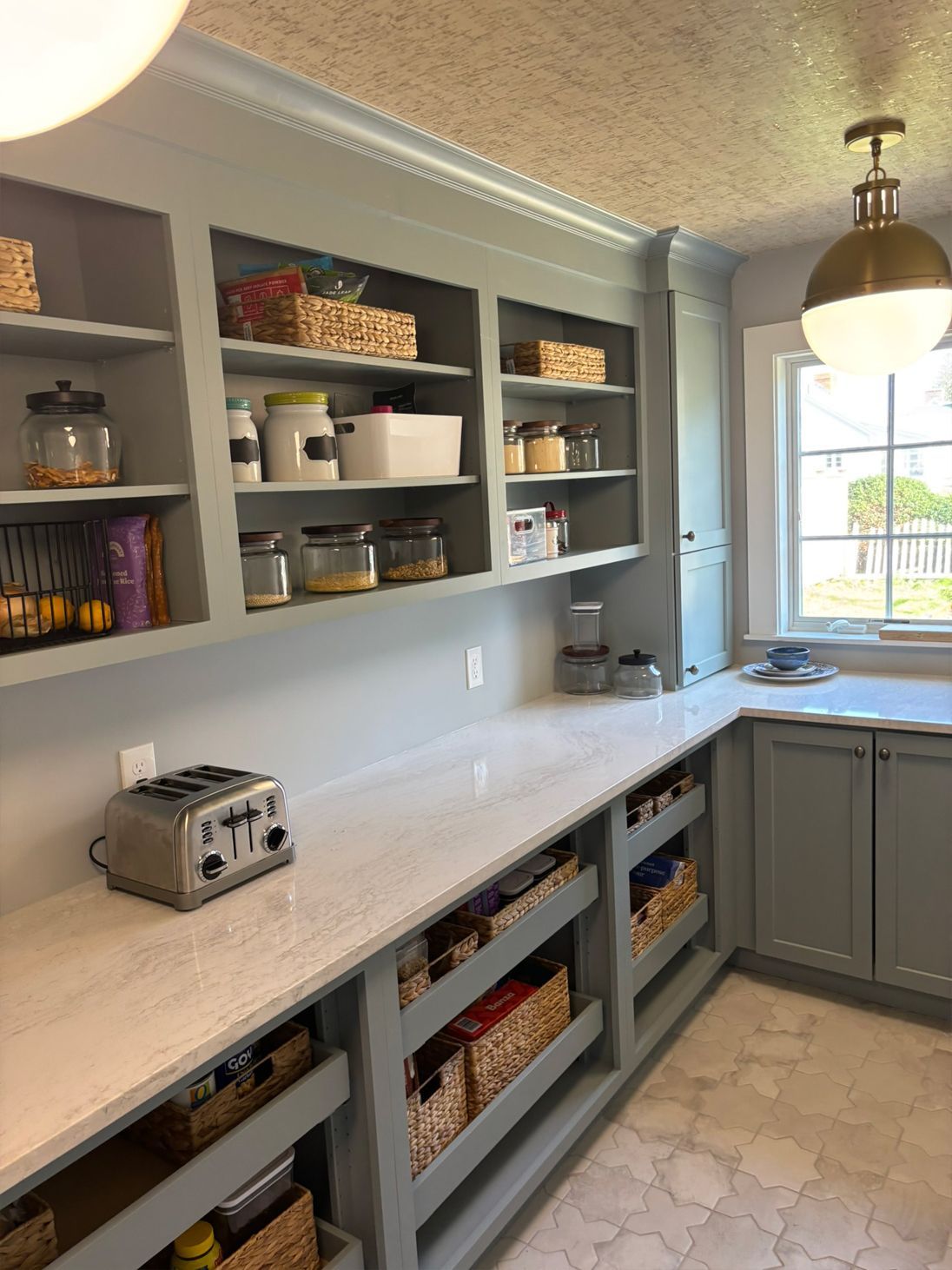Light blue pantry with built-in shelves, countertop, and baskets, a toaster, and a gold-toned light fixture.