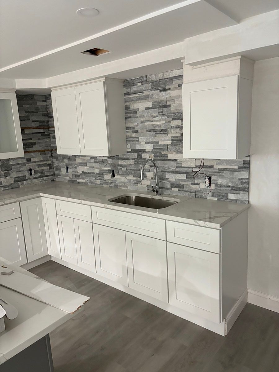 A newly remodeled kitchen with white cabinets, a sink, and a stone wall