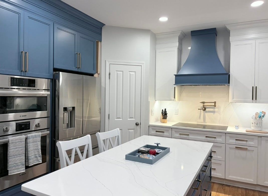 A modern kitchen features a blue island, blue upper cabinets, a custom blue range hood, and white countertops.