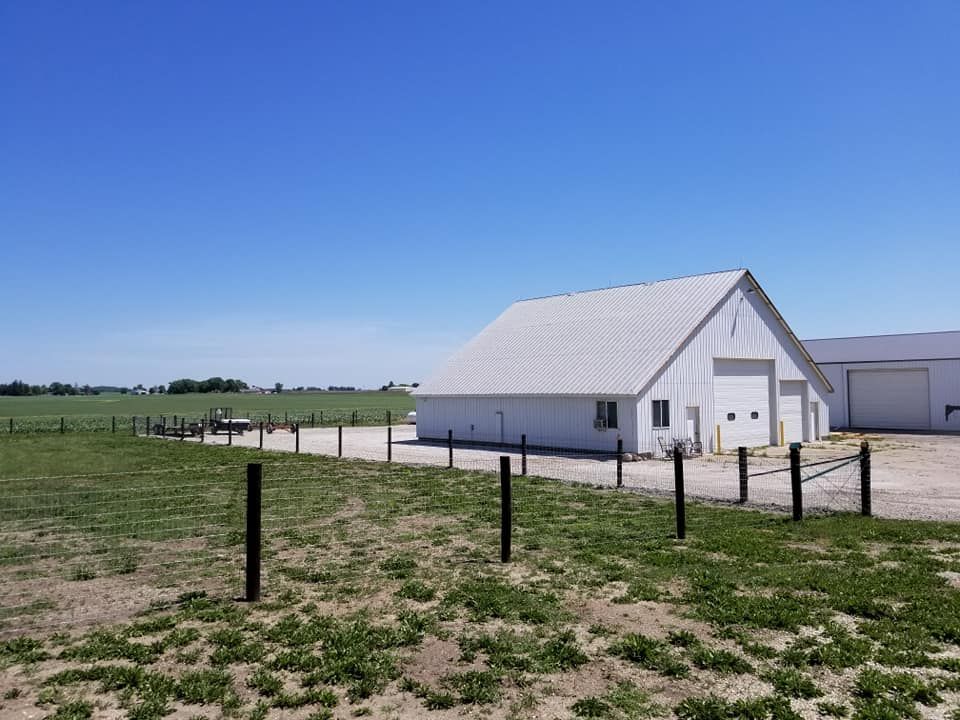 A white barn is sitting in the middle of a grassy field.