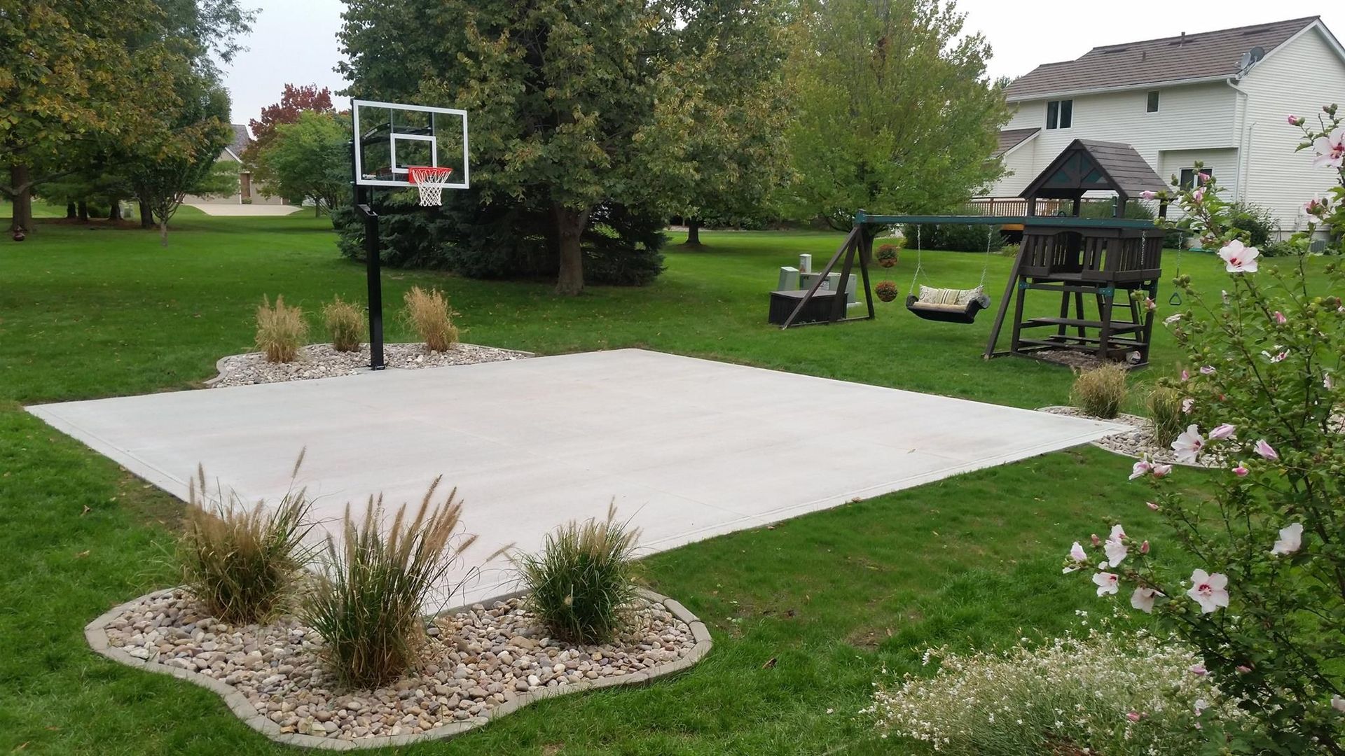 A basketball hoop is in the middle of a lush green yard.
