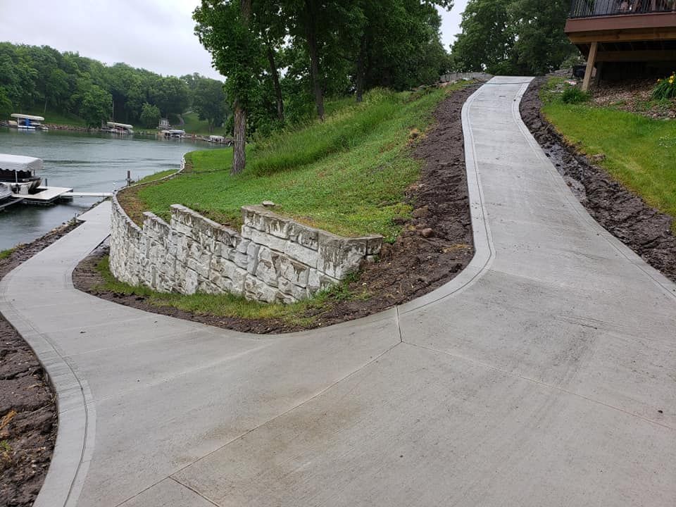 A concrete driveway leading to a lake with a boat docked in the background.