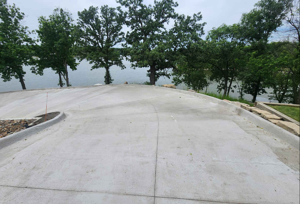 A concrete driveway leading to a lake surrounded by trees