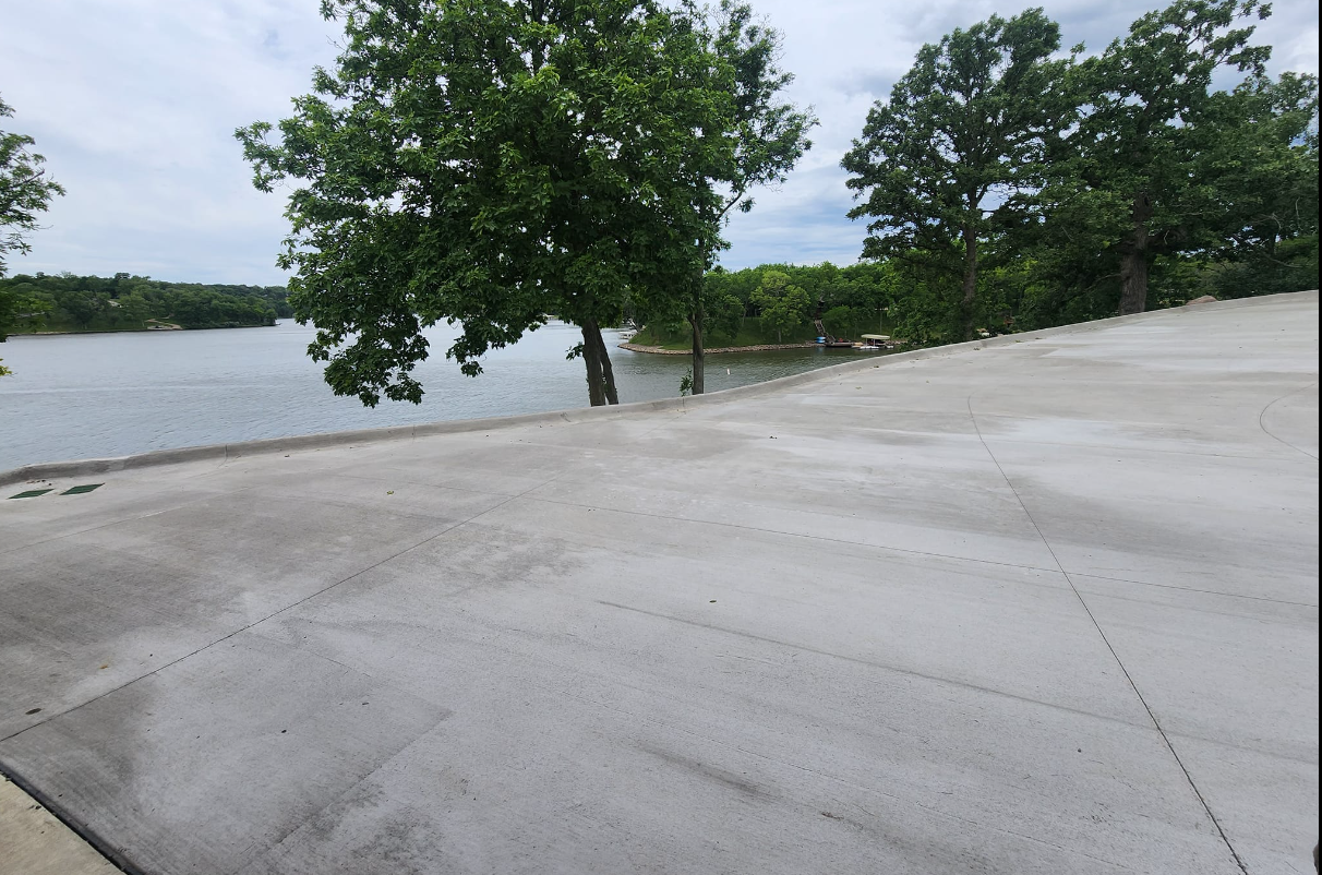 A concrete driveway leading to a lake with trees in the background