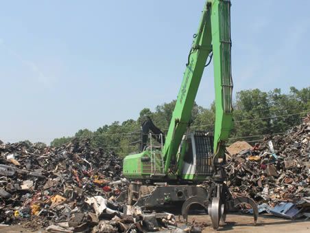 A green crane is standing in front of a pile of scrap metal.