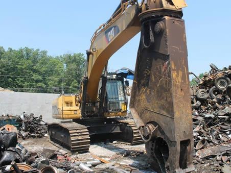 A cat excavator is working on a pile of scrap metal.