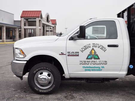 A white recycling truck is parked in front of a building