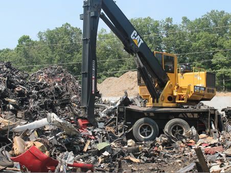 A yellow cat crane is in a pile of scrap metal