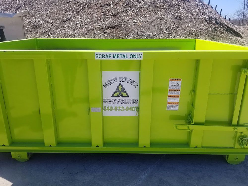 A green dumpster is sitting in front of a pile of gravel.