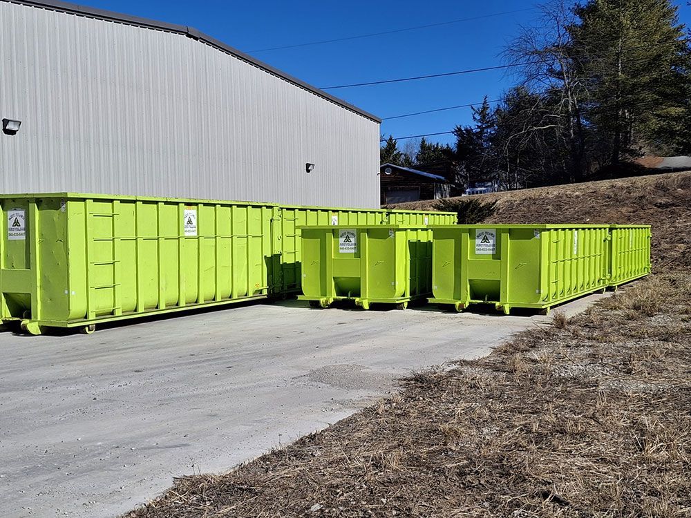 A row of green dumpsters are parked in front of a building.