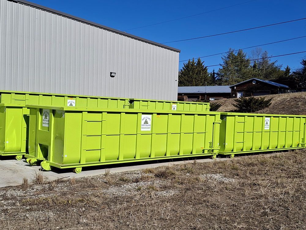 A bunch of green dumpsters are sitting in a field in front of a building.