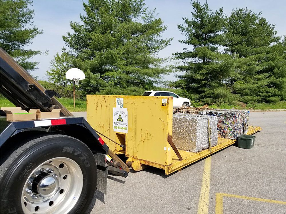 A dumpster is being towed by a truck in a parking lot