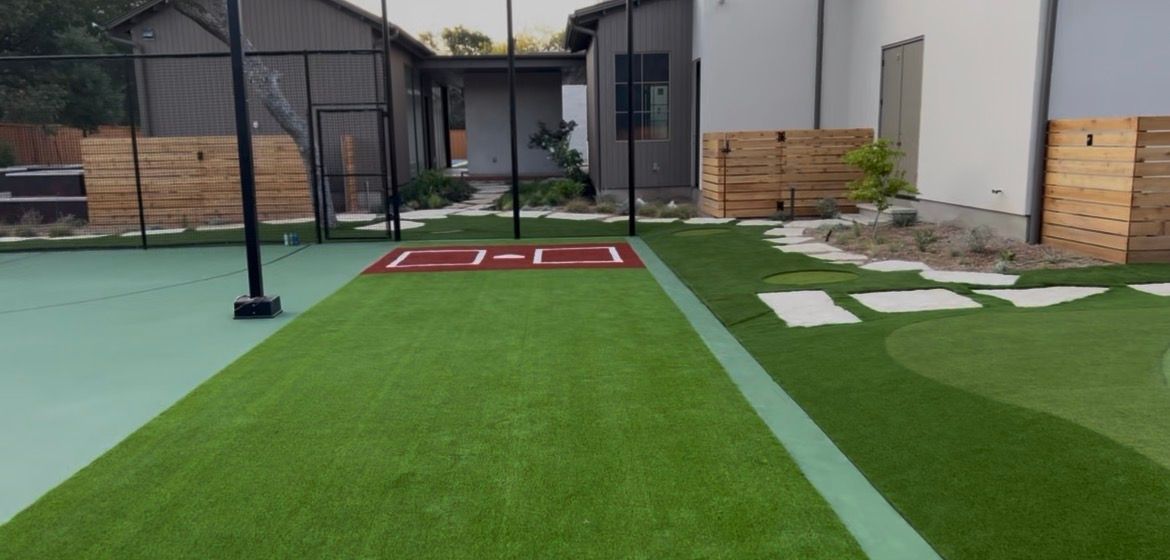 Artificial turf training area with a black pole, red mat, and wall padding by a building