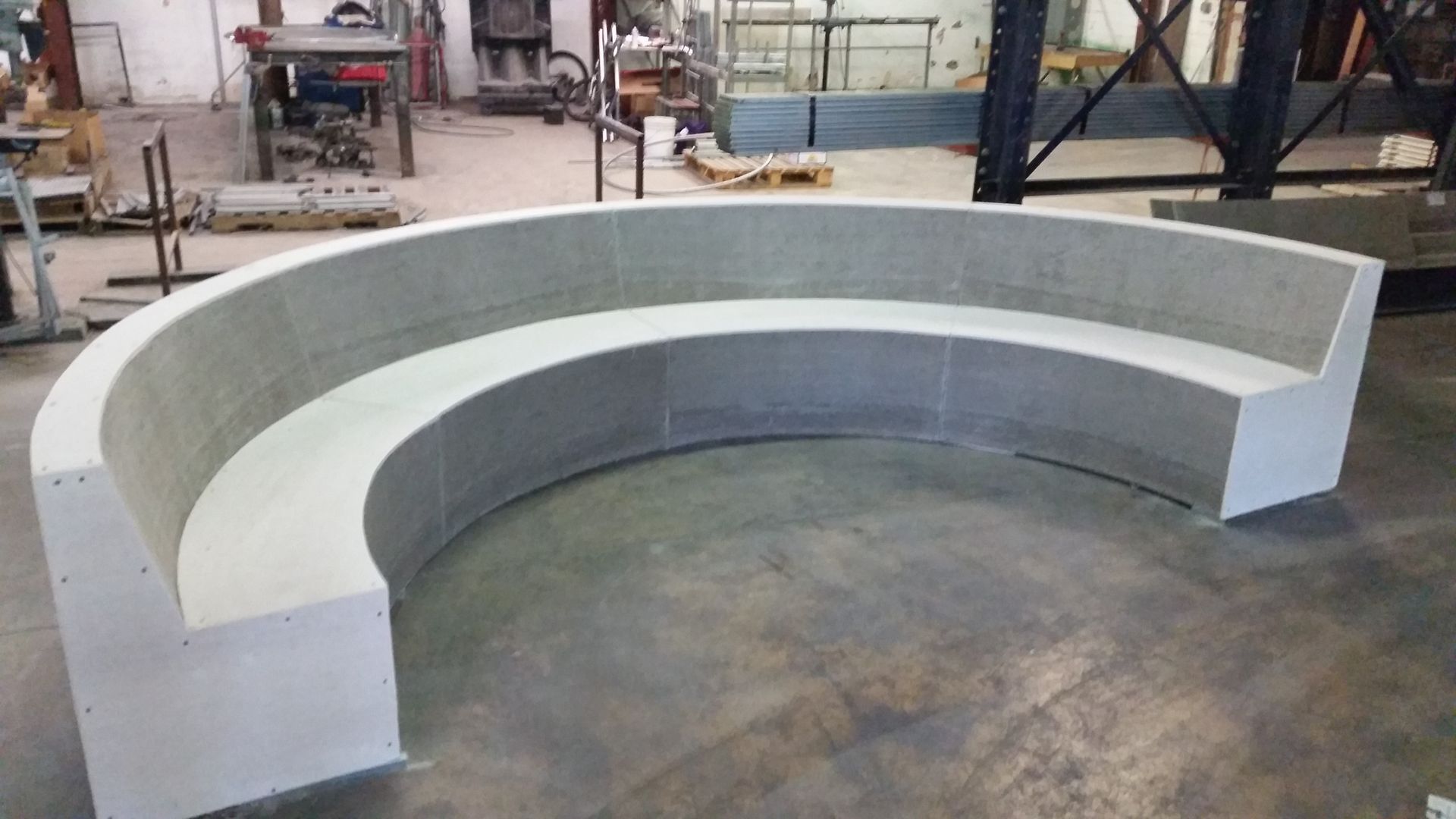 A curved concrete bench is sitting on a concrete floor in a factory.
