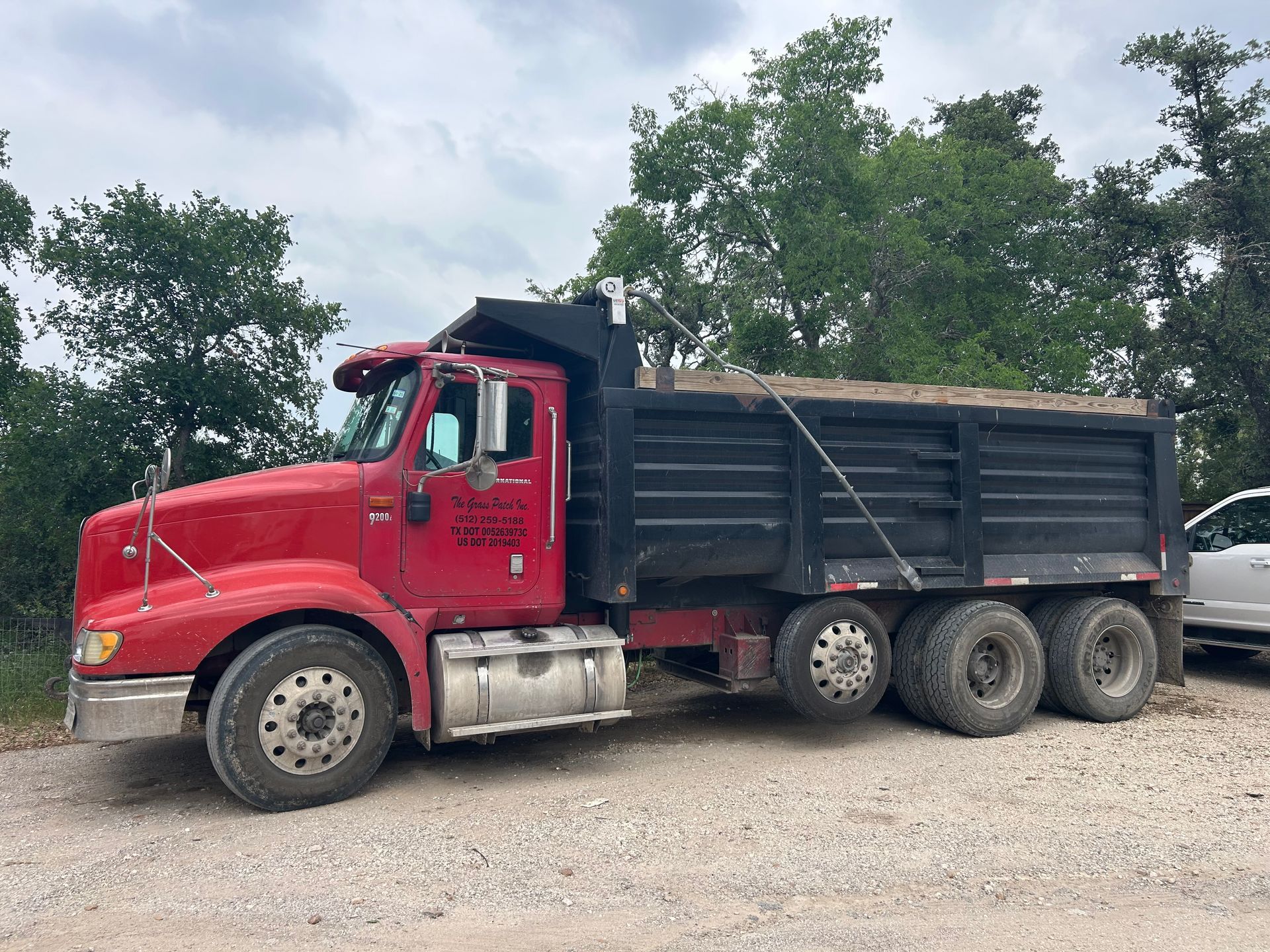 A red dump truck is parked in a gravel lot next to a white truck.