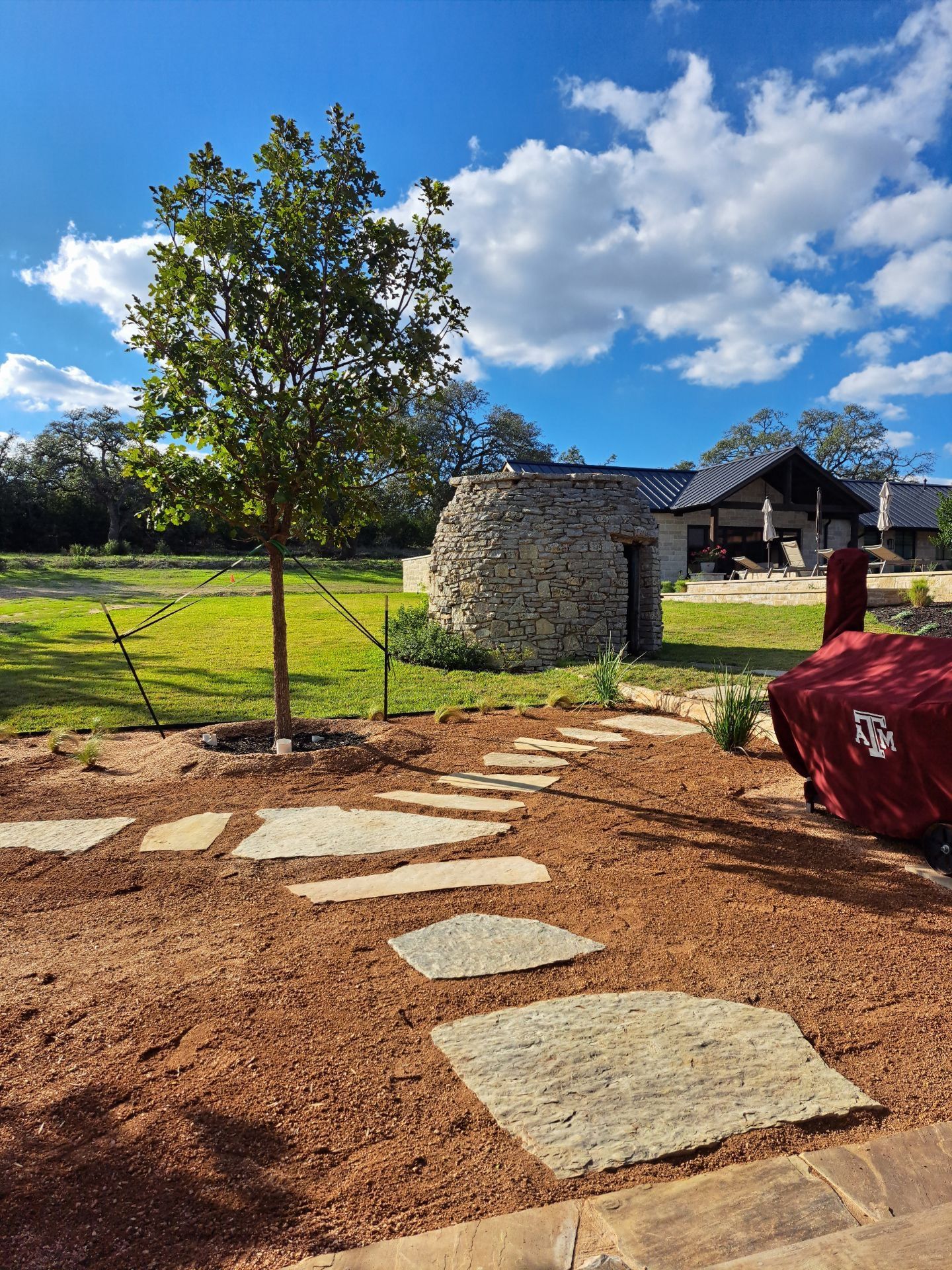 A stone walkway leading to a house with a stone building in the background.