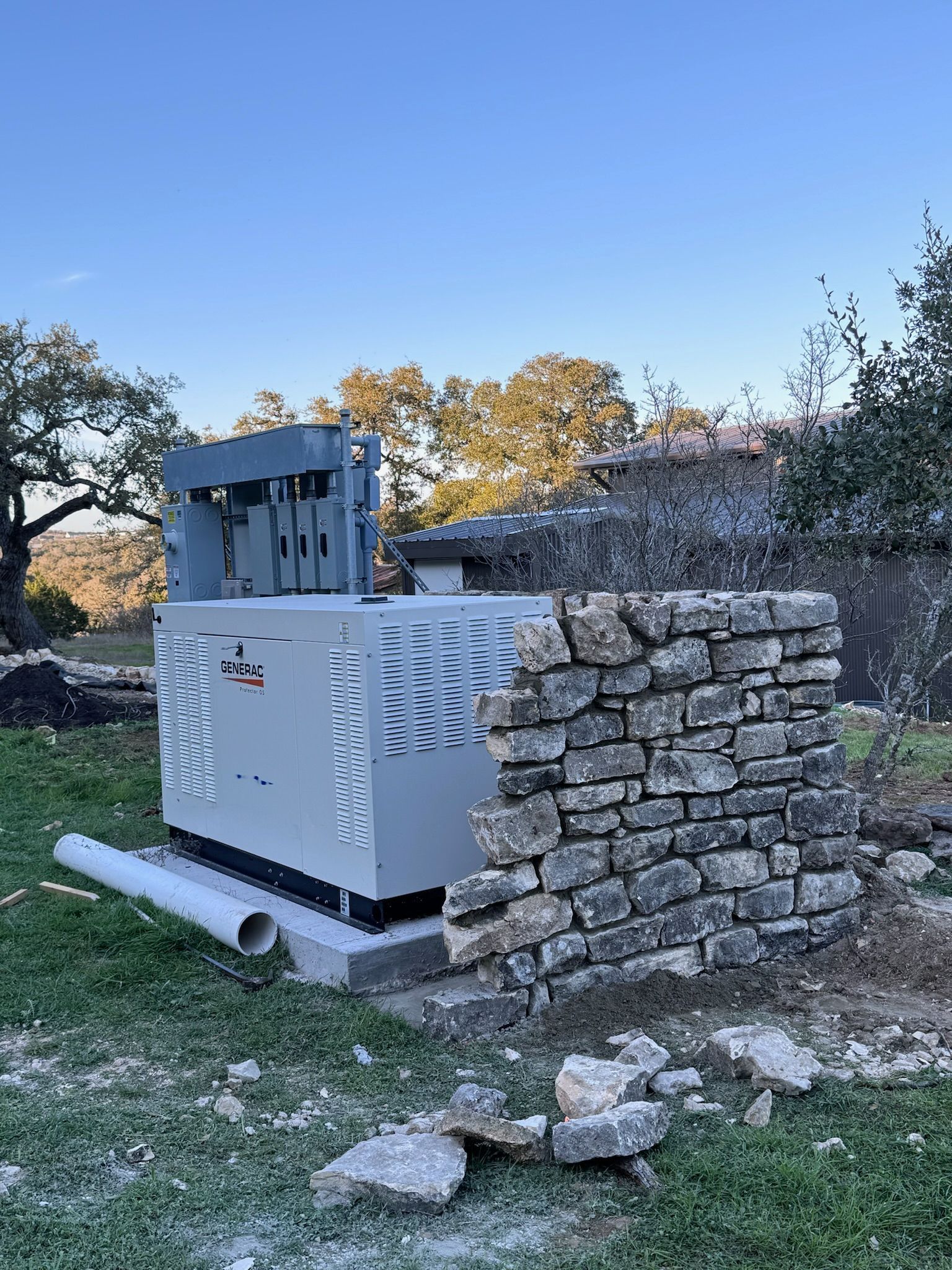 A generator is sitting in the grass next to a stone wall.