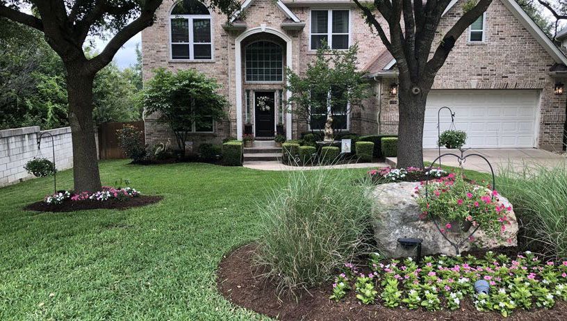 A large brick house with a lush green lawn and flowers in front of it.