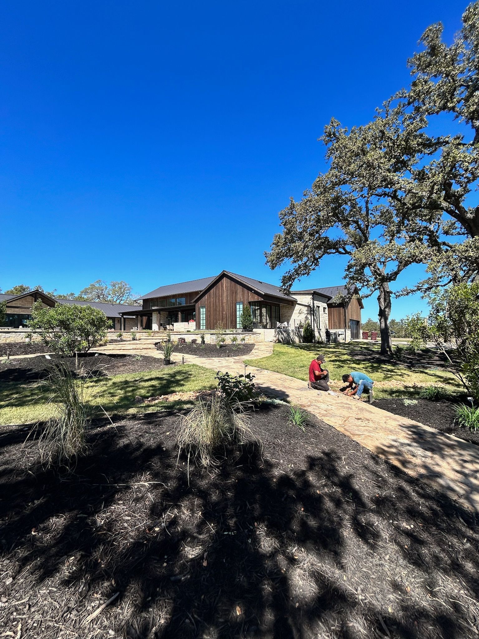 A man is working in a garden in front of a large house.