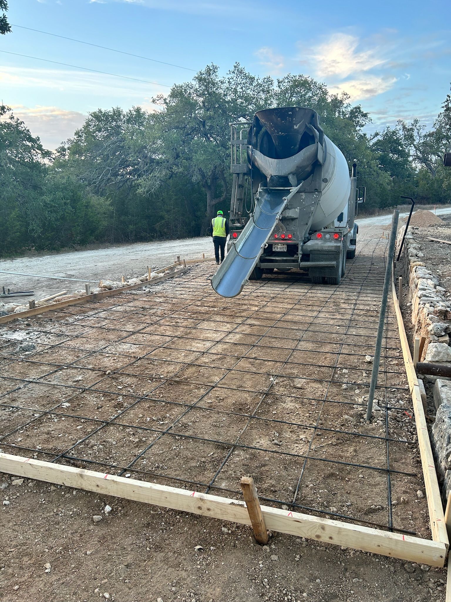 A concrete mixer truck is pouring concrete on a dirt road.