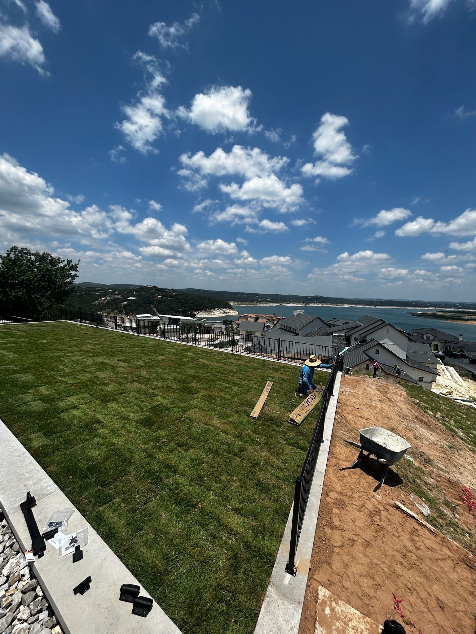 A large lawn with a wheelbarrow in the foreground and a large body of water in the background.