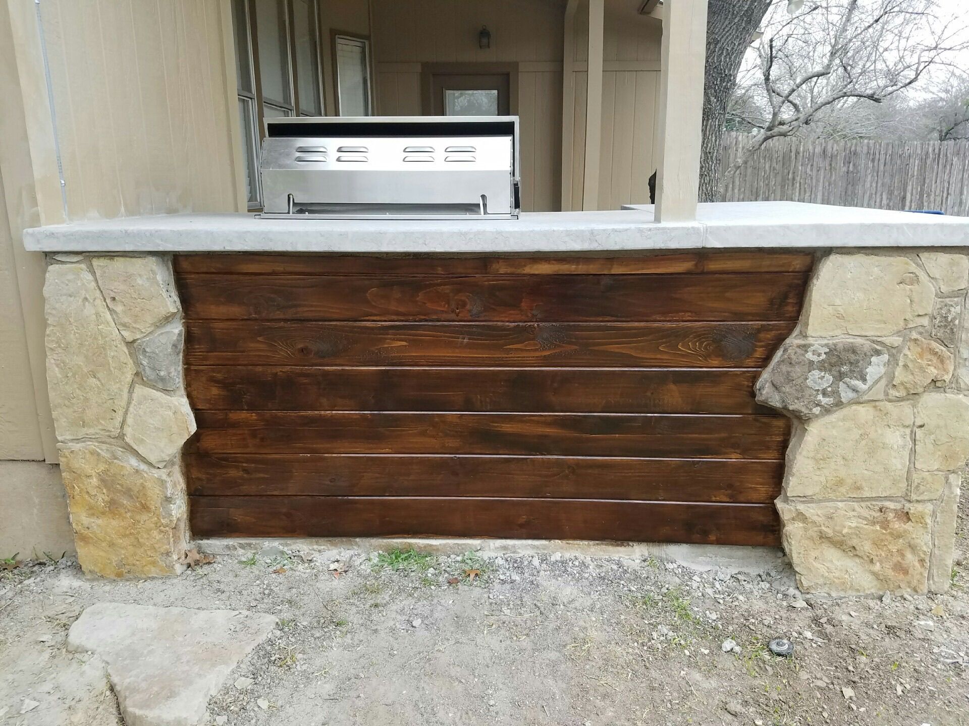 A grill is sitting on top of a wooden wall next to a stone wall.