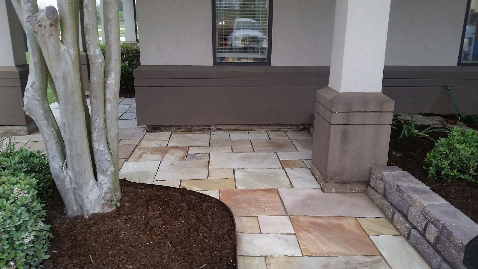 A stone walkway in front of a building with a tree in the foreground
